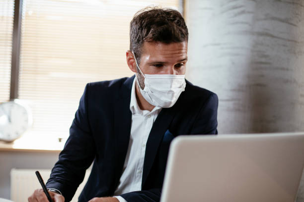 istock Young businessman with a mask working in his office on laptop. 1301348856