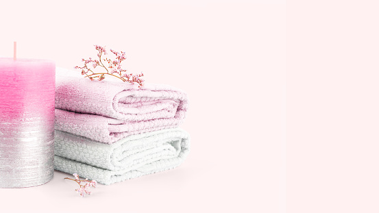 Textured decorative aroma candle, bath towels and branches of delicate wildflowers on a pale pink background. Soft pastel spa composition. Soft focus. Copy space.
