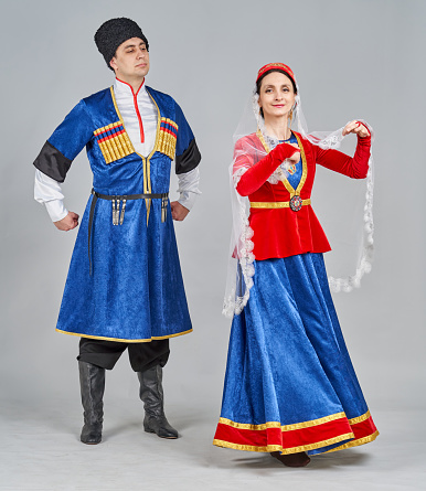 Two dancers (middle-aged caucasian woman and young man native of Central Asia) are dressed in a Georgian traditional clothing. The dancers are dancing Georgian folk dance and showing traditional poses. They are smiling. Studio shooting