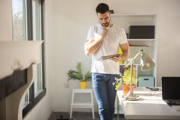istock Young entrepreneur standing in living room and using tablet 1301355510