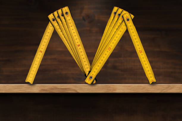folding ruler in the shape of letter m on a wooden shelf - folding ruler imagens e fotografias de stock