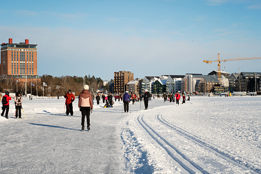 Vasteras, Sweden - February 6 2021: Beautiful sunny winter day in the city. People are cross country skiing, going for a walk,  and ice skating on the frozen lake.