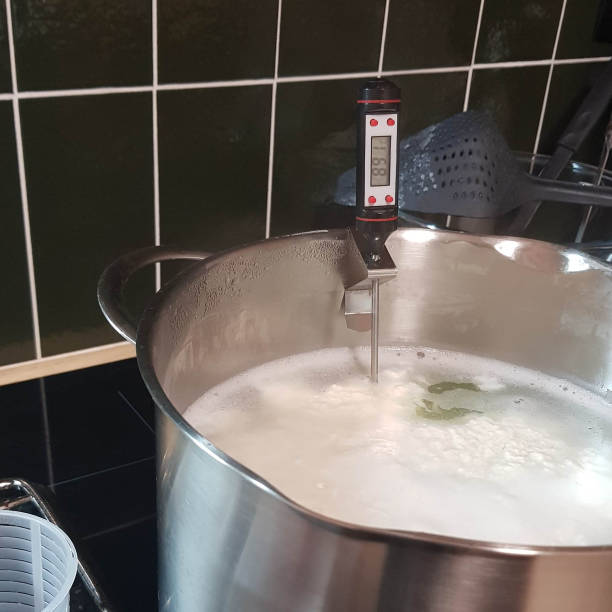istock Making cheese ricotta with your own hands. Step-by-step photos of the process. Formation of cheese flakes of ricotta clouds in whey in a saucepan with a thermometer. Square stock photo. 1301361310
