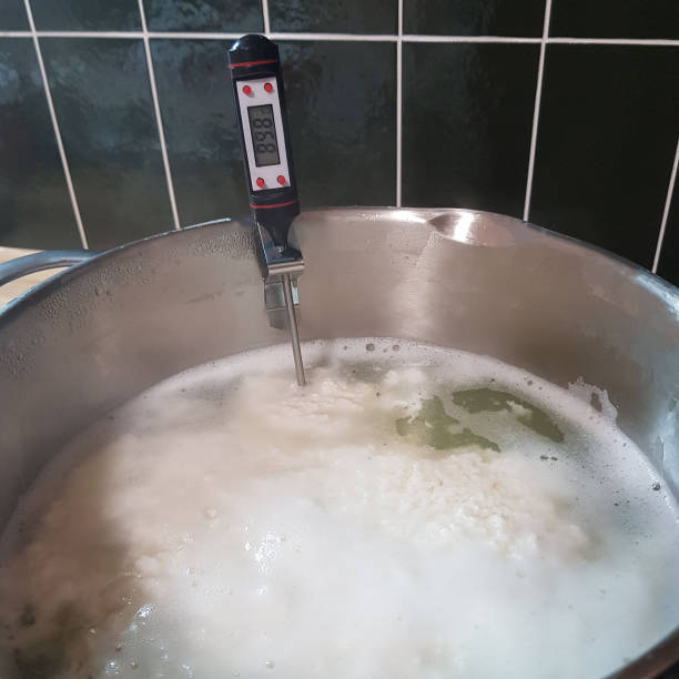 istock Making cheese ricotta with your own hands. Step-by-step photos of the process. Formation of cheese flakes of ricotta clouds in whey in a saucepan with a thermometer. Square stock photo. 1301361316