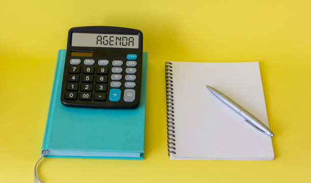 istock Agenda word, text on calculator, multicolored notepad on yellow background 1301362407