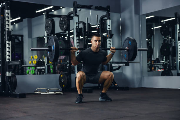 istock A side portrait of a bodybuilder in grey doing squats using a barbell in a gym to train his legs and back. Powerful fitness workout 1301364373
