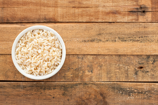 Top view of white bowl full of boiled brown rice over wooden table