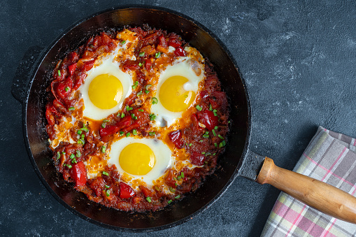 Shakshuka, fried eggs with tomatoes, onion, red pepper and spices in cast iron pan, close up