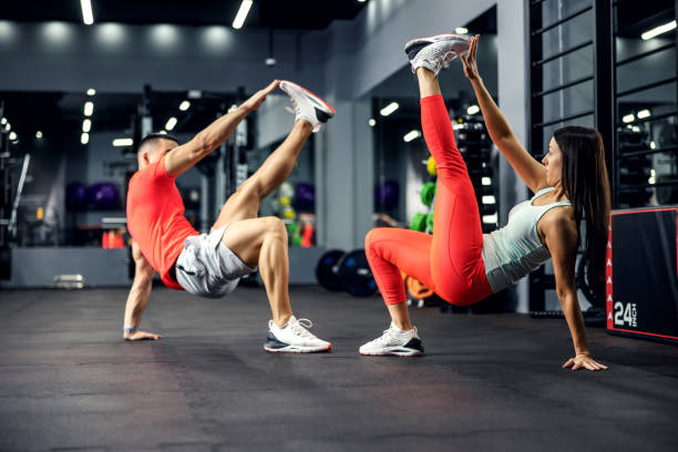istock The athletic strong couple performs an acrobatic exercise for the core in the gym with a big mirror and black mat. They stay strong and balanced. Relationship fitness goal, sport lover 1301366536