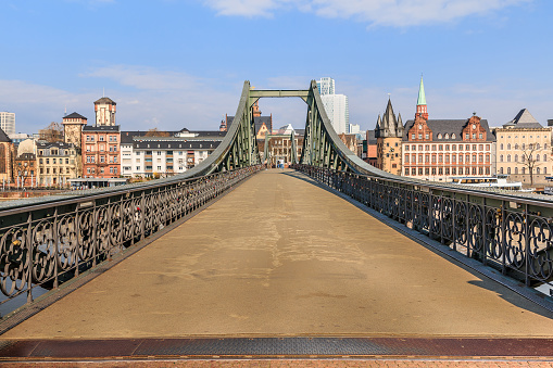 Historic footbridge over the Main in Frankfurt. Houses of the old town in the background with sunshine and a few clouds. Bridge with iron terrain