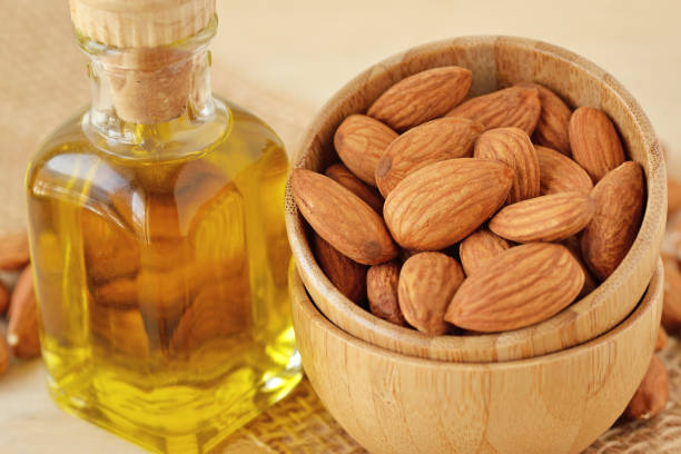 Bottle of almond oil and almonds in wooden bowl stock photo