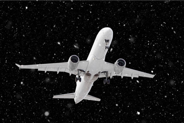 istock white passenger plane has released its landing gear and is landing through falling snow against background of dark night in winter 1301380133