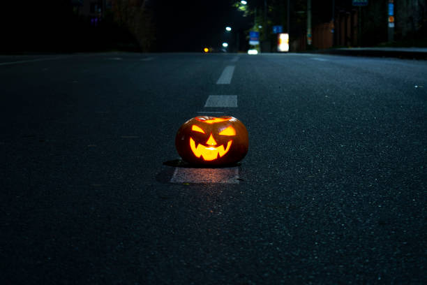 Halloween pumpkin with carved demonic face and candle inside. festive  beautiful pumpkin on a night asphalted road. Night photo.