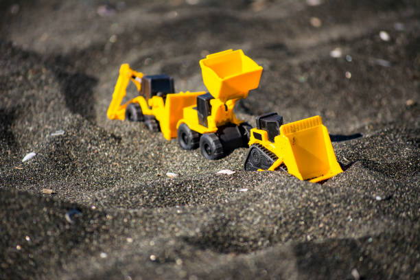Toy construction machinery in black sand. Yellow and black colors toy machines. Bulldozer, loader, excavator.