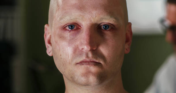 Unhappy crying young man with dropping tears on the face. Closeup studio portrait on grey background. Negative emotional concept. Toned dark shadow color