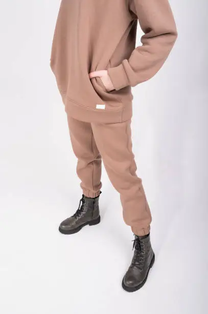 Cropped view of young woman in taupe hoodie and stylish coarse boots isolated on white. Beige female sweatshirt sweatshirt and pants with blank label. Streetstyle clothes concept. High quality photo