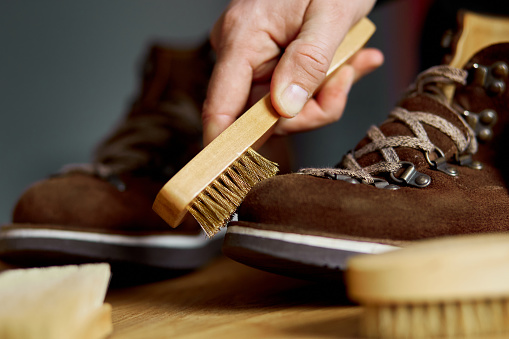Man's hand clean suede shoes, boots with a brush on wooden background. Footwear maintenance captured, copy space, for text.