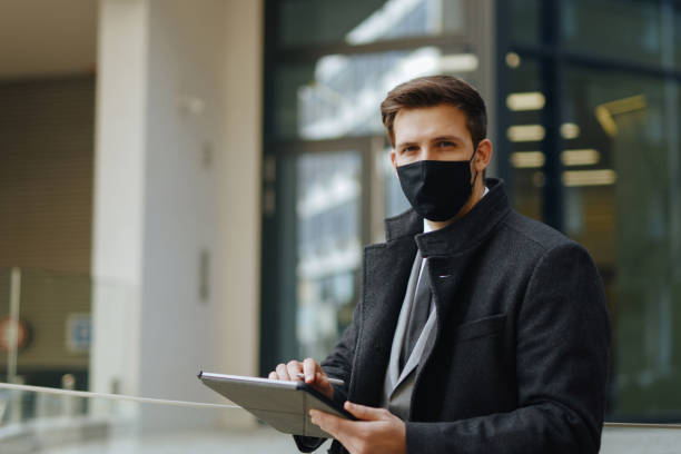 istock Mid adult businessman with protective face mask working on digital tablet 1301386049