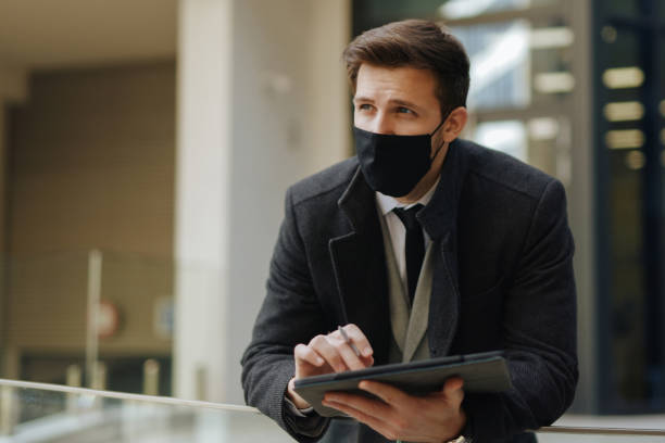 istock Mid adult businessman with protective face mask working on digital tablet 1301386104
