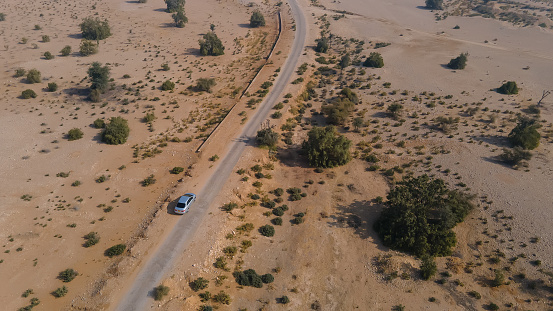 Jamshoro, Pakistan - January 15, 2021: Aerial view of silver car driving on country road in desert. Shot from drone flying over road.