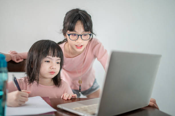 istock asian chinese young girl attending online class at the kitchen dining table with help from her sister 1301389568