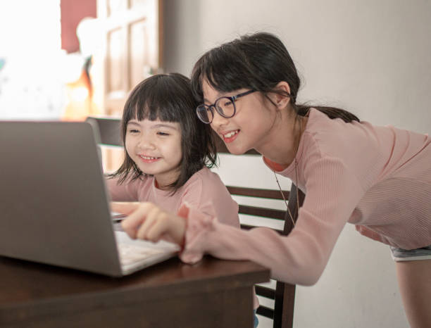 istock asian chinese young girl attending online class at the kitchen dining table with help from her sister 1301389583