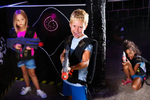 Emotional preteen boy with a laser pistol playing laser tag with friends at dark labyrinth