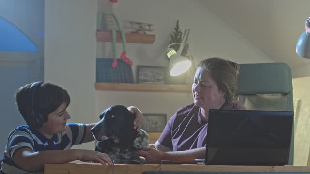 The pet sits next to the landlady and her son at the table in front of the laptop