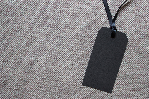 Blank black paper label on textured striped fabric. Photo with copy blank space.