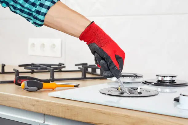 Repairs and fixing of gas control panel. Man hand in protective gloves repairs hotplate of a hob.