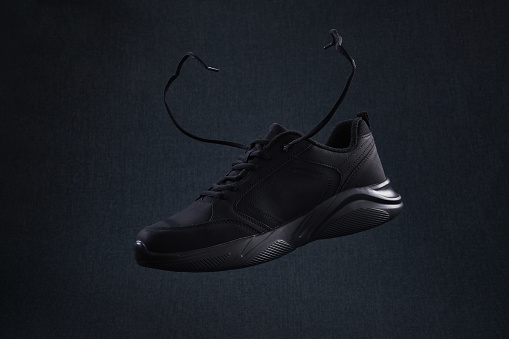 Fashion black unbranded sneaker with laces flying on dark background. Black sport running shoes levitate in the air.