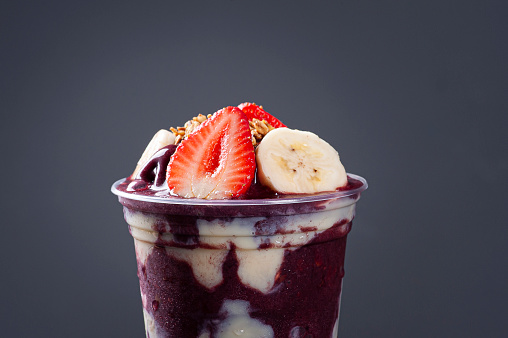 Brazilian frozen açaí in a plastic cup with condensed milk, banana and strawberry. Fruit from the Amazon. Copy space