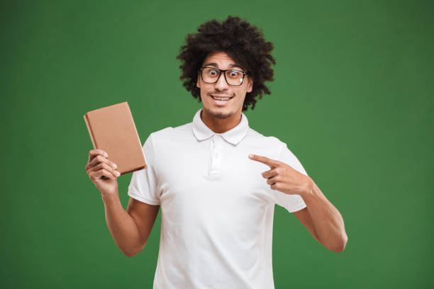 istock Happy young african curly man holding book pointing. 1301395340