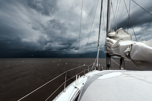 White sailboat in the North Sea under dramatic storm clouds. Near Horumersiel, District of Friesland, Lower Saxony, Germany.