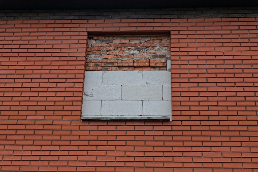 red wall of an unfinished house with a window covered with white bricks