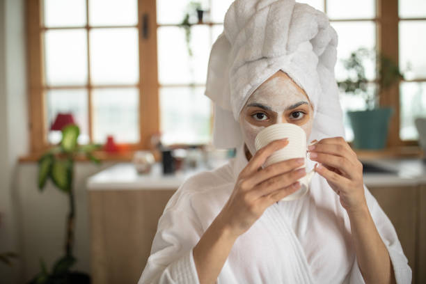 joven bebiendo café y relajándose en casa - bathrobe women cup towel fotografías e imágenes de stock