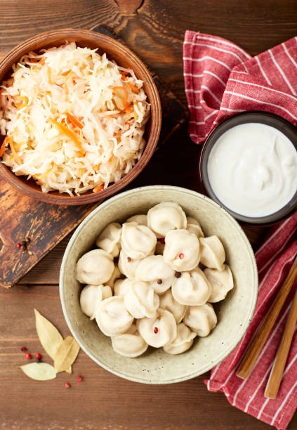 Dumplings stuffed with meat, pelmeni, ravioli, dumplings. Traditional Russian pelmeni dumplings with sour cream and sauerkraut with sour cream over wooden background. Top view, flat lay. russian pelmeni stock pictures, royalty-free photos & images