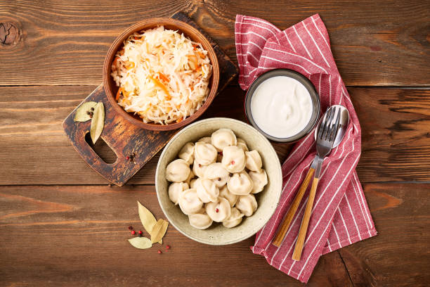 Dumplings stuffed with meat, pelmeni, ravioli, dumplings. Traditional Russian pelmeni dumplings with sour cream and sauerkraut with sour cream over wooden background. Top view, flat lay. russian pelmeni stock pictures, royalty-free photos & images