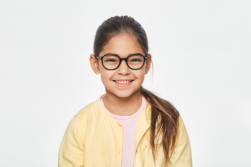 Beautiful Latin American little girl in stylish red glasses on light gray background