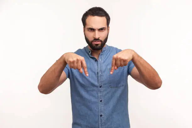 Photo of Serious bossy man with beard pointing fingers down commanding to act here and now, demanding immediate result