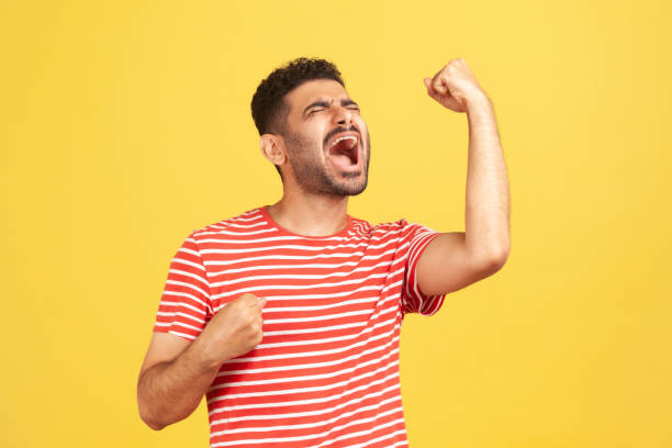 istock Extremely excited overjoyed man with beard in striped t-shirt shouting making yes gesture, amazed with his victory, triumph 1301401633