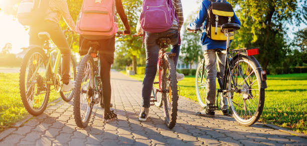 niños con mochilas montando en bicicleta en el parque cerca de la escuela - andar en bicicleta fotografías e imágenes de stock