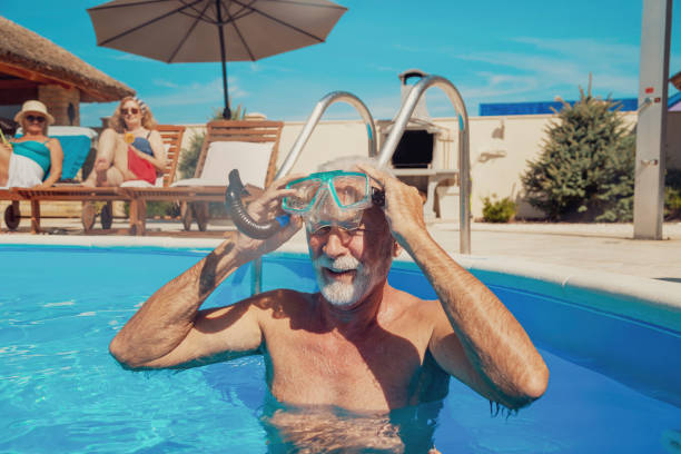 Senior man snorkeling in the swimming pool Group of senior friends relaxing and sunbathing by the swimming pool, enjoying summer vacation; elderly man putting on snorkel mask, having fun snorkeling in the pool vacation rental mask stock pictures, royalty-free photos & images