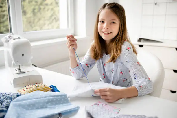 Photo of pretty girl is sitting by the table in her parents office embroidering, doing needlework