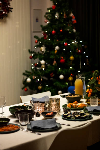istock Christmas dinner table set for four with linen tablecloth and line napkins, salmon dish, sushi. Christmas thee in the background. Real life festive table setting. 1301407773