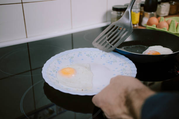 istock Preparing eggs for breakfast. Overhead view of black kitchen stove with frying pan. 1301409300