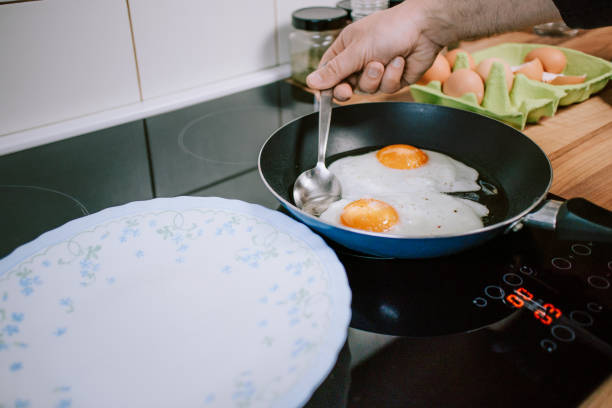 istock Preparing eggs for breakfast. Overhead view of black kitchen stove with frying pan. 1301409320