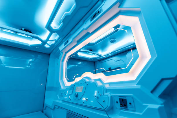 istock Inside a small cozy room in a capsule hotel - a futuristic interior with a light control panel, electric charging and an alarm clock filled with calm blue light 1301415678