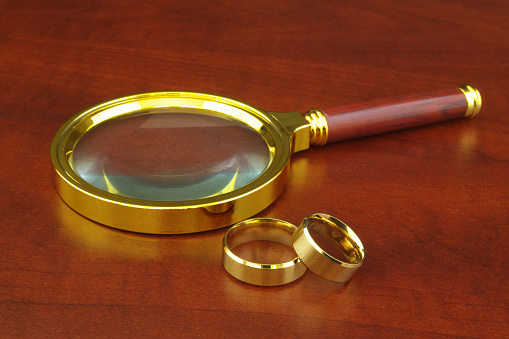 Golden wedding rings and magnifying glass on wooden table.