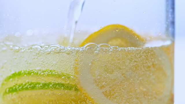 SLO MO LD Pouring sparkling water into a glass with lemon and lime slices